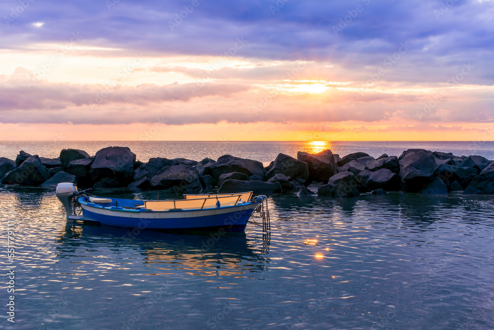 boat in morning or evening sea with rock pier and amazing sunrise or sunset with nice clouds on background of landscape