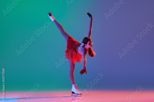 Young sportive girl, junior female figure skater in red stage costume skating isolated over gradient green-blue background in neon light. Grace, beauty, winter sports photo