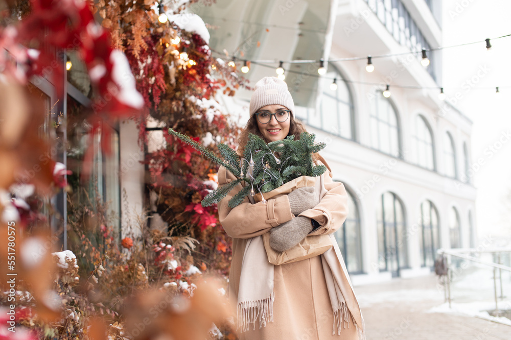 Stylish young woman with branches of nobilis walks through the Christmas city