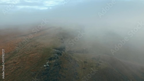 Large bare rocky cliffs, outcrop with small  dense white fog and grey clouds. natural cliff, aerial drone view of morning mists moving slowly over the rugged Pennine hills, on a foggy morning. photo