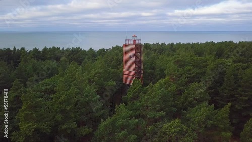 Aerial view of Bernati lighthouse surrounded by lush green pine tree forest, Nordic woodland, Baltic sea coast, sunny autumn day, Latvia, wide angle orbital drone shot photo