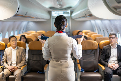 Asian flight attendant is demonstrating safety procedure using seat belt before taking off in the airplane for cabin crew and airline business concept