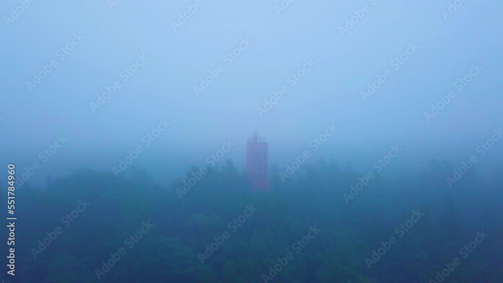 Aerial view of Bernati lighthouse surrounded by lush green pine tree forest, Nordic woodland with thick mist, Baltic sea coast, foggy autumn day, Latvia, wide angle drone shot moving forward Aerial view of Bernati lighthouse surrounded by lush green pine tree forest, Nordic woodland with thick mist, Baltic sea coast, foggy autumn day, Latvia, wide angle drone shot moving forward