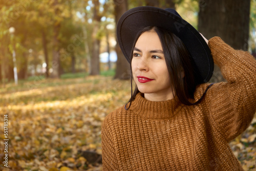 portrait of attractive stylish smiling woman with long hair walking in park dressed in warm brown coat autumn trendy fashion, street style wearing hat © Yurii