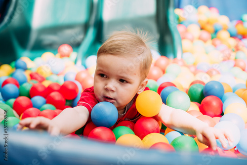 Happy laughing boy 1-2 years old having fun in ball pit  in kids amusement park and indoor play center. Activity toys for little kid