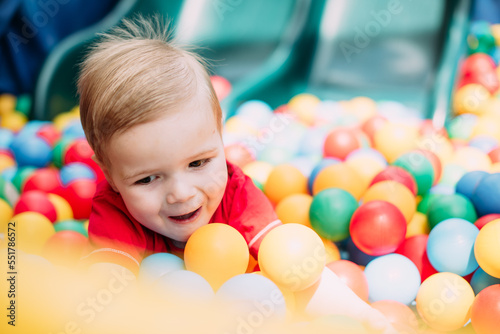 Happy laughing boy 1-2 years old having fun in ball pit  in kids amusement park and indoor play center. Activity toys for little kid