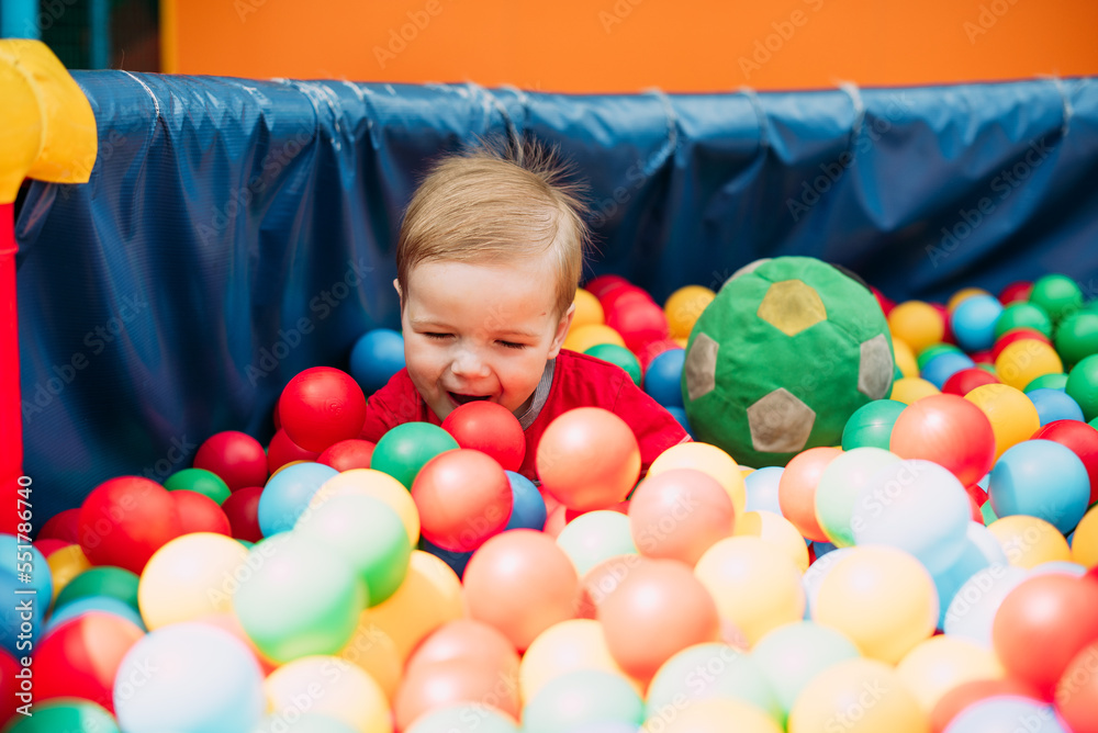 Obraz premium Happy laughing boy 1-2 years old having fun in ball pit in kids amusement park and indoor play center. Activity toys for little kid