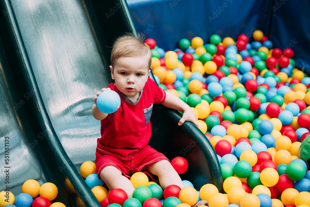 Obraz premium Happy laughing boy 1-2 years old having fun in ball pit in kids amusement park and indoor play center. Activity toys for little kid