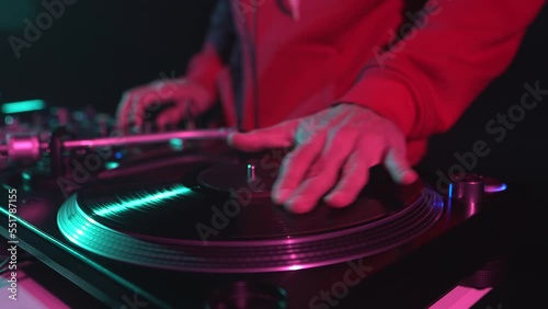 Party DJ scratches vinyl disc on turntable. Hip hop disc jockey scratching records and playing music in night club