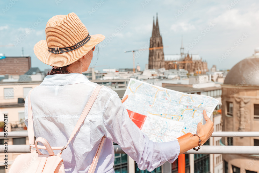 Tourist girl with maps, navigating for sights and landmarks and geolocating on the streets of an old European city. Cologne cathedral in the background