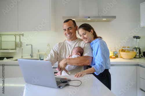 Happy parents with newborn child using laptop in kitchen