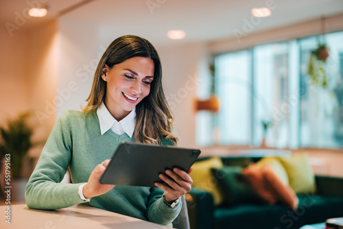 Smiling businesswoman surfing the web over the digital tablet, sitting in the living room, elegantly dressed.