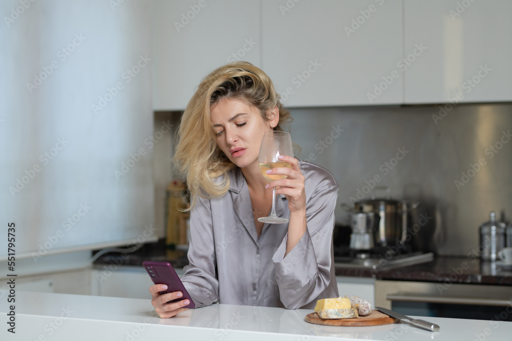 Beautiful girl with phone drinking wine in kitchen. Morning of pretty woman housewife. Beautiful girl with phone drinking wine in kitchen. Morning of pretty woman housewife.