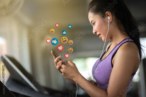 Asian woman enjoy using smartphone addiction to technology trends following with icons on social networks after exercise in gym. Social medias and technology concept.