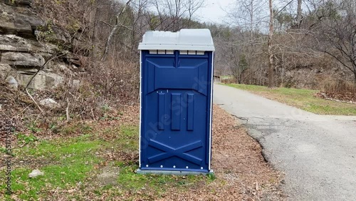 static video of a blue porta potty in a park with dead trees and asphalt roads. 4k photo