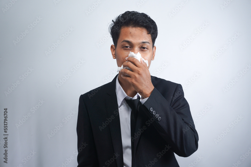 Horizontal portrait of unhealthy handsome man wearing suit, blowing nose into tissue. Male have flu, virus or allergy against white background. Healthy medicine and people concept Horizontal portrait of unhealthy handsome man wearing suit, blowing nose into tissue. Male have flu, virus or allergy against white background. Healthy medicine and people concept
