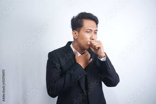 Man in suit coughing into his fist, isolated on a gray background.