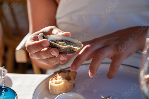 Young woman in white dress eats fresh live oysters seafood in French restaurant