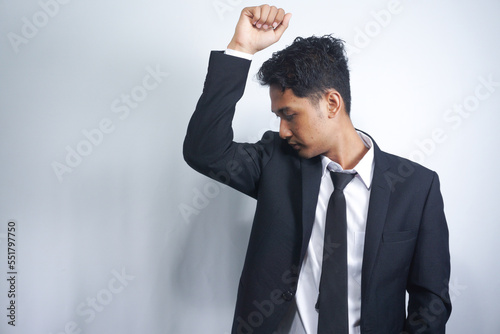 A man smells his underarm through his suit. Checking for signs of body odor from his armpit. His Antiperspirant is working. Isolated on a white background.