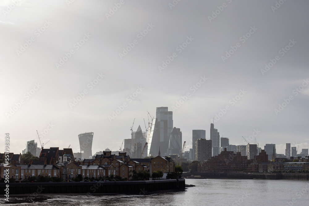 Fototapeta premium London dockland housing on the River Thames waterfront and modern business buildings in the background, handheld shot. Fusion of traditional and contemporary architecture concept.