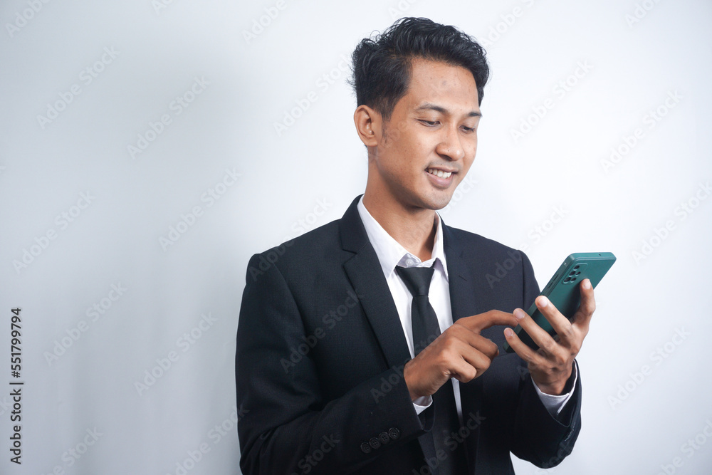 Portrait of a happy Asian young man wearing a suit while pointing at a mobile phone Portrait of a happy Asian young man wearing a suit while pointing at a mobile phone