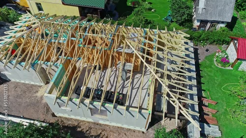 Aerial drone rotating shot over wooden frame of roof structure under construction in a suburban neighborhood on a bright sunny day. photo
