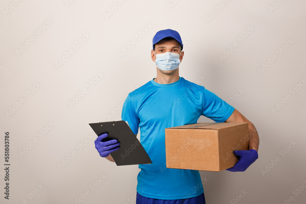 Portrait of handsome attractive delivery man in a medical mask and gloves holding card-board box. Express delivery service. Copy space. Portrait of handsome attractive delivery man in a medical mask and gloves holding card-board box. Express delivery service. Copy space.
