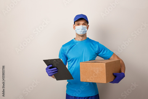 Portrait of handsome attractive delivery man in a medical mask and gloves holding card-board box. Express delivery service. Copy space.