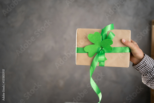 Hand of a young man holding a gift box with green ribbon on a gray background. Present for St.Patricks day photo