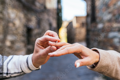 Cropped image of a man's hand placing an engagement ring on his future wife's finger in a stone alley.