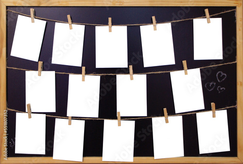 White Paper sheets hanging on the rope on wooden clothespins. Set of Blank notes on blackboard in a wooden frame. 14 empty notes on a black background. Mock up template. Real photo.