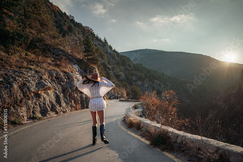 The woman is dear to the mountains. A woman in a white sweater, black boots and a hat walks along a winding alpine path between the mountains at the end of summer at sunset. Travel concept.