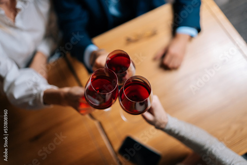 Fotografía Close-up top view of unrecognizable man and women clinking glasses with red wine during festive dinner at table in luxury restaurant at evening