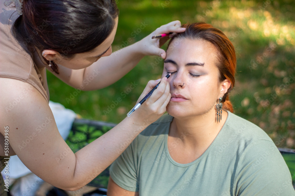 Profesional maquillando a la modelo preparada para la sesión de fotos en un parque de Madrid con los árboles de fondo desenfocados. Profesional maquillando a la modelo preparada para la sesión de fotos en un parque de Madrid con los árboles de fondo desenfocados.