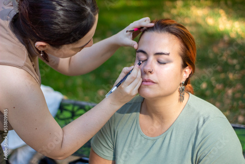 Profesional maquillando a la modelo preparada para la sesión de fotos en un parque de Madrid con los árboles de fondo desenfocados.