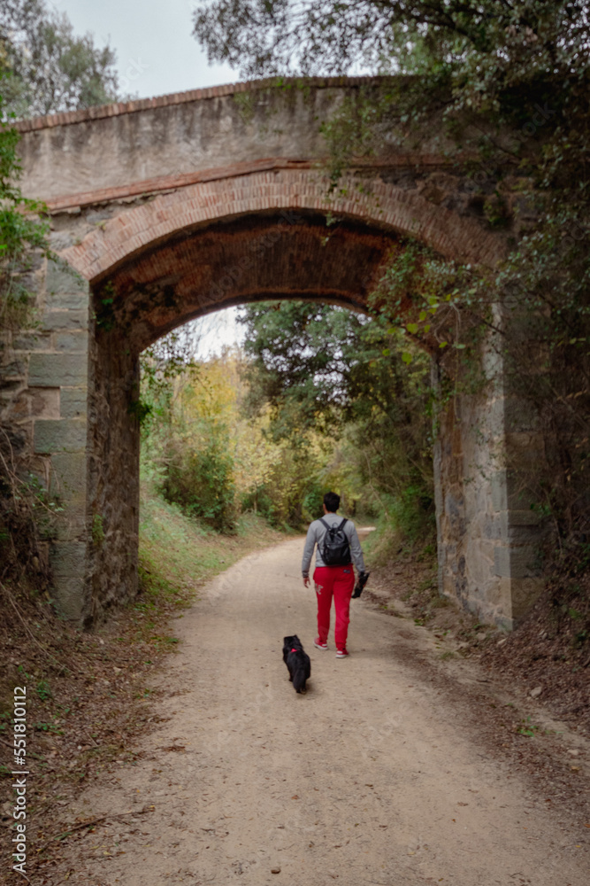 Senderista paseando con el perro por la ruta de la montaña pasando por debajo del puente con su mochila para pasar el día en la naturaleza.