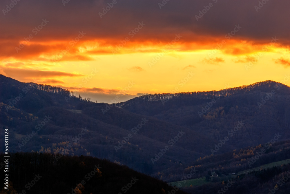 Mountain landscape with forest after sunset. Fiery sky in orange yellow. View of the valley. Late autumn. Dubrava, Slovakia.