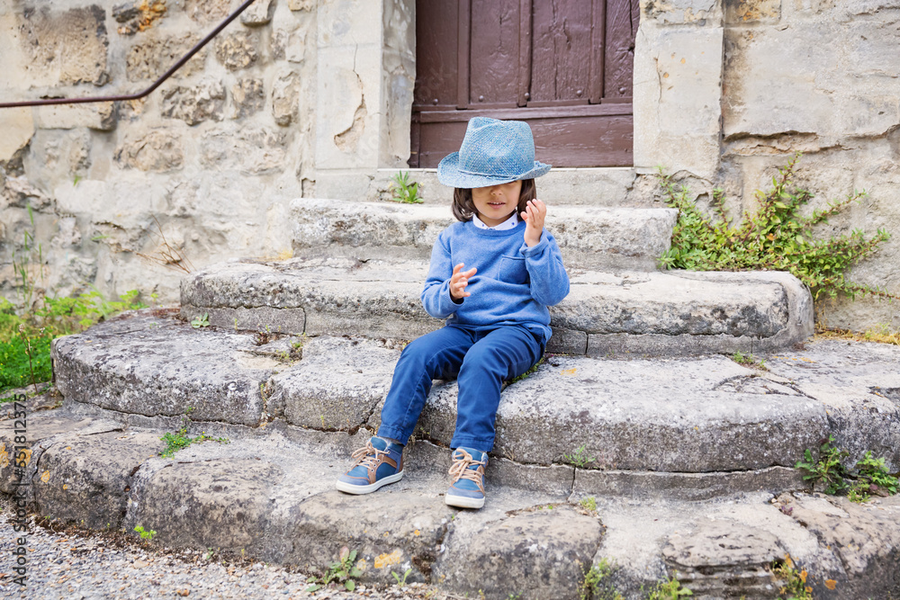 Little handsome baby boy sitting on ancient stone stairs and playing outdoor with straw hat in old city Little handsome baby boy sitting on ancient stone stairs and playing outdoor with straw hat in old city
