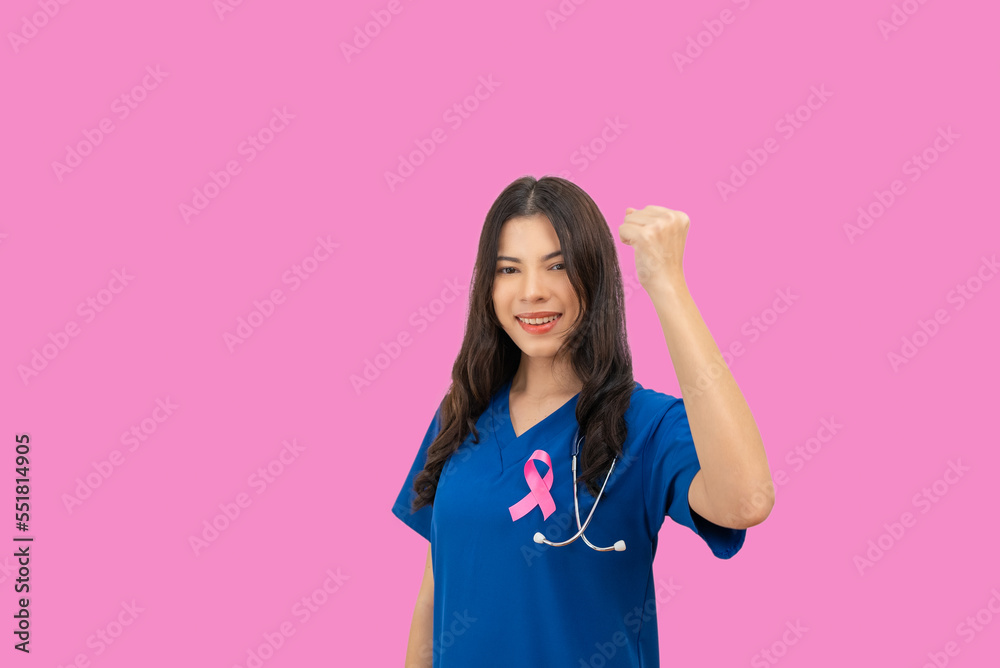 Doctor nurse woman in blue uniform stuck pink ribbon symbolizing World Cancer Day on the chest, raise her hands to fight Breast Cancer on pink background. Doctor nurse woman in blue uniform stuck pink ribbon symbolizing World Cancer Day on the chest, raise her hands to fight Breast Cancer on pink background.