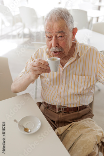  un signore anziano vestitocon camicia seduta al tavolino di un bar sorseggia un buon caffè photo