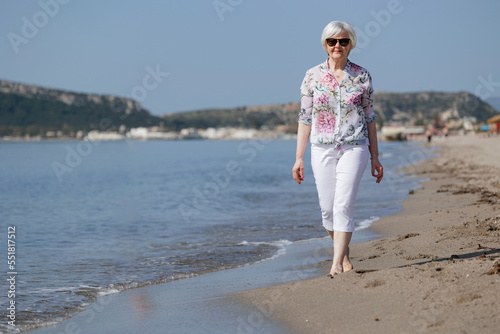 bella signora anziana passeggia in riva al mare, sullo sfondo si vede la spiaggia le montagne photo