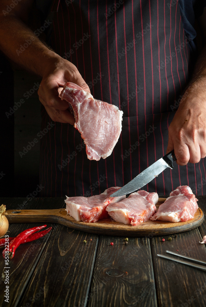 The cook with a steak in his hand in the restaurant kitchen before preparing a delicious lunch or grill. Advertising space on a dark background