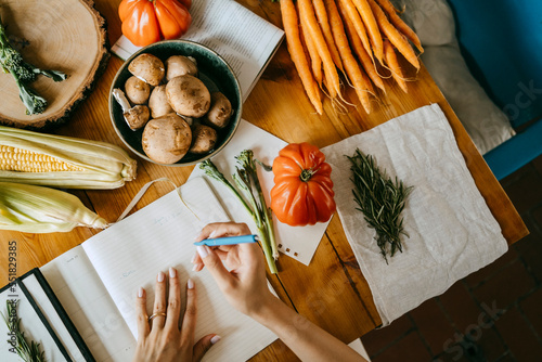 Directly above view of food stylist writing in diary amidst vegetables on table photo