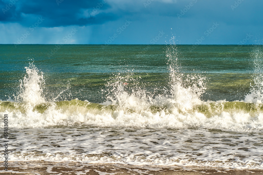 Fototapeta premium Small sea waves with splashes of water flying up on the coast. A relaxing holiday on the beach. Memories of a summer vacation.