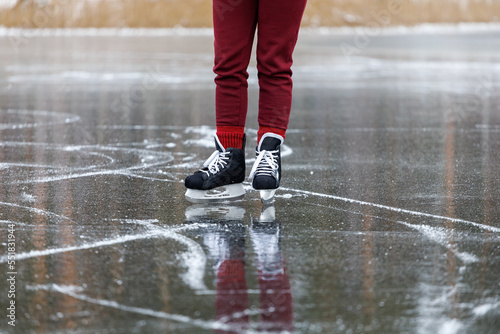 Black skates on ice. Women's legs in burgundy pants stand on the surface of a frozen forest lake