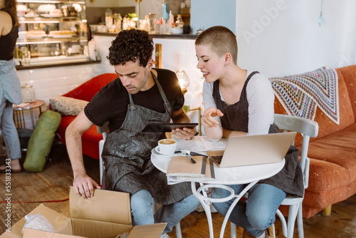 Male and female owners checking box while sitting on chair in cafe photo