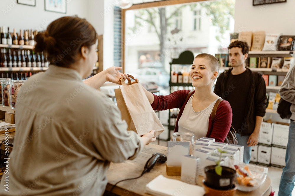 Young happy female customer taking paper bag from owner at checkout counter in store Young happy female customer taking paper bag from owner at checkout counter in store
