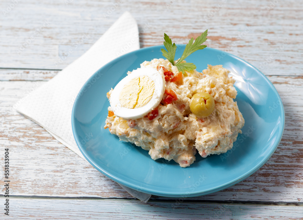 Tapa of russian salad on a blue plate on a wooden background Tapa of russian salad on a blue plate on a wooden background