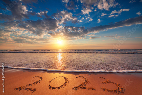 Happy New Year 2023 concept, lettering on the beach sand. Celebration and golden ocean sunrise