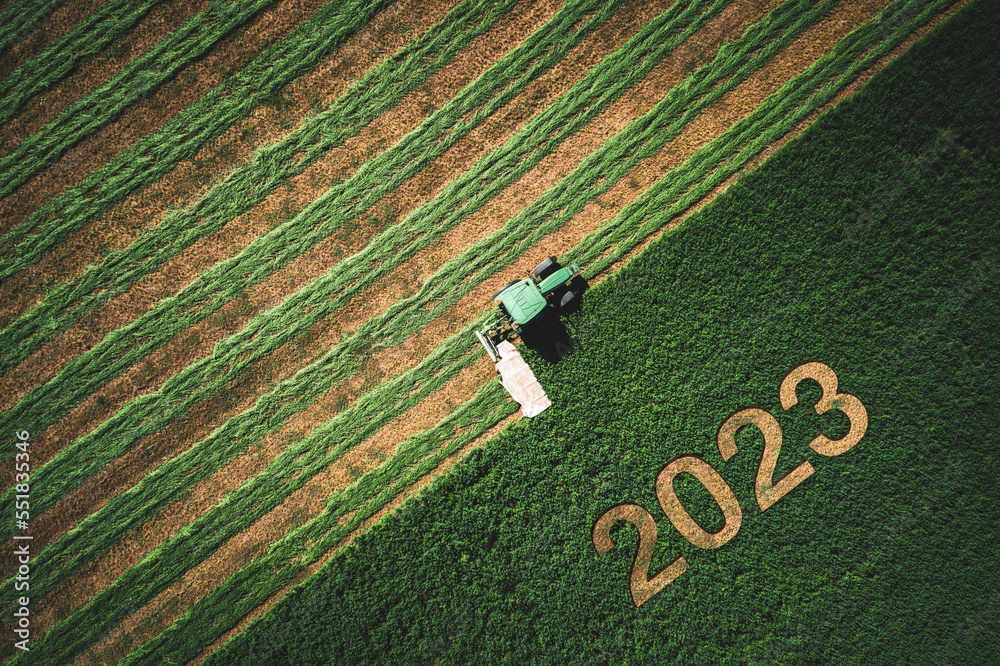 2023 Happy New year concept for agriculture, business, goals, success and new start banner. Industrial tractor on a green field. - obrazy, fototapety, plakaty 